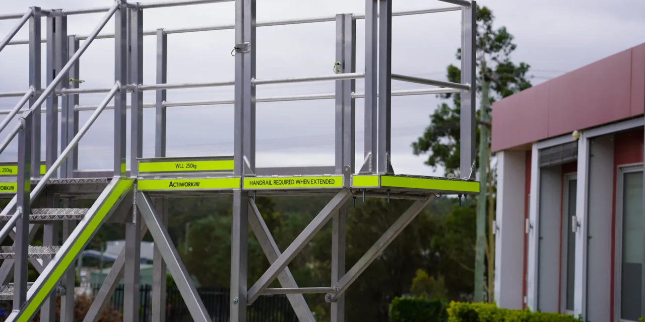 Adjustable industrial access platform with handrails and stair access for safe maintenance and elevated work environments.